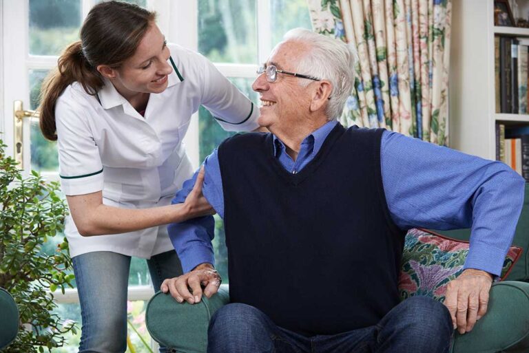 Older couple shares a meal in an accessible assisted living apartment while a caregiver provides discreet support.